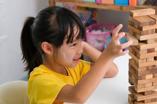 Cute Asian siblings having fun playing Jenga together. Two children playing Jenga board game on table in room at home. Wooden puzzles are games that increase intelligence for children. Educational toys for children.