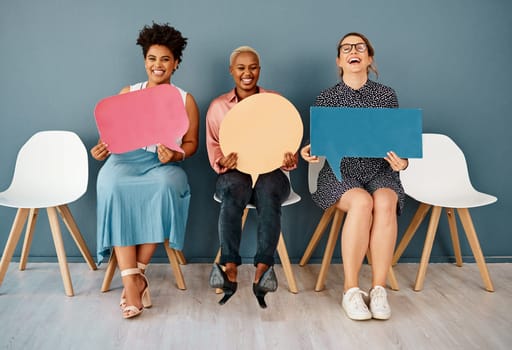 Isnt that just funny. Studio portrait of a group of attractive young businesswomen holding speech bubbles while sitting in a row against a grey background