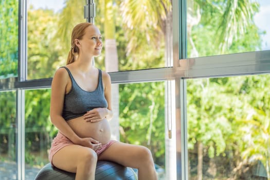 Pregnant woman exercising on fitball at home. Pregnant woman doing relax exercises with a fitness pilates ball. Against the background of the window.