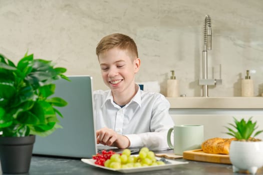 young boy, teenager plays on the notebook during breakfast time. Addiction to gadgets. Breakfast before school in the kitchen.