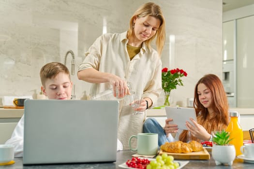 Young family with school kids have fun at breakfast time. Happy family eating healthy breakfast. Quality time with Family in kitchen eating together. Family Using Digital Devices At Breakfast