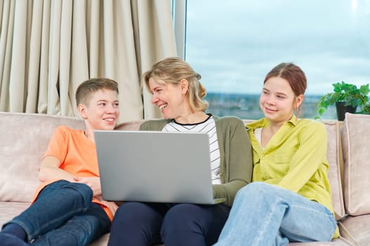 Happy family with kids sit on sofa in living room have fun using laptop together, smiling parents rest on couch enjoy weekend with childrens laugh watch video on computer at home