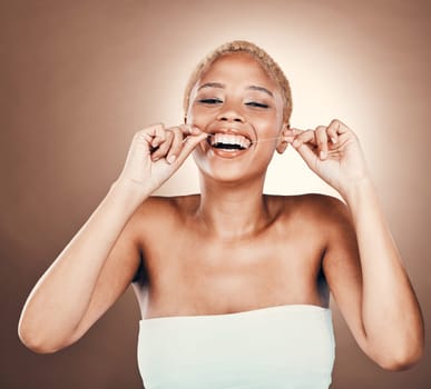 Teeth, dental floss and portrait of black woman on a brown background for healthy smile. Aesthetic model person laughing in studio for self care, cleaning mouth and hygiene for health and wellness.