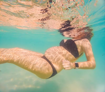 Pregnant woman underwater swimming in tropical sea. Healthy and active pregnancy. Young expecting mom on summer beach vacation before baby birth. Swim holiday and water fun. Travel during pregnancy. Underwater photography.