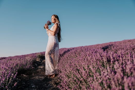 Close up portrait of young beautiful woman in a white dress and a hat is walking in the lavender field and smelling lavender bouquet.