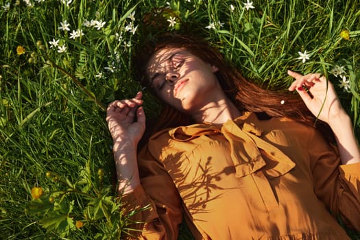 a relaxed woman, resting lying in the green grass, in a long orange dress, with her eyes closed and a pleasant smile on her face, recuperating, illuminated by the warm rays of the setting summer sun. High quality photo