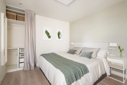 Stylish bright bedroom with a bedside table and a double bed and an empty wardrobe for things with beige wallpaper and cute pictures on the wall. The concept of an apartment for a young family.