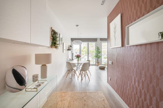 View from the entrance hall to a stylish living room with a round dining table, TV and panoramic windows and decorative accessories. Concept of a modern city apartment for a young family.