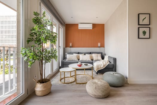 Stylish seating area with a terracotta color wall with a sofa and pouffes near the panoramic windows in the living room. The concept of a modern Scandinavian interior.