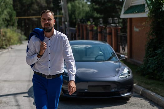 Attractive bearded man in a blue suit near a black car in the countryside in summer