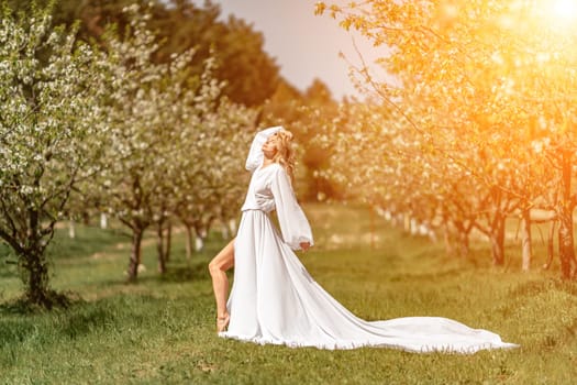 Blond blooming garden. A woman in a white dress walks through a blossoming cherry orchard. Long dress flies to the sides