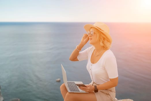 Freelance women sea working on the computer. Good looking middle aged woman typing on a laptop keyboard outdoors with a beautiful sea view. The concept of remote work