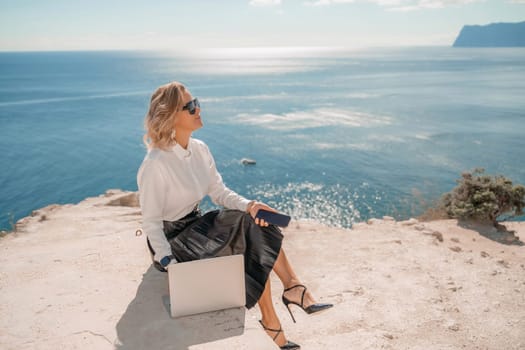 Freelance women sea working on a computer. Pretty middle aged woman with computer and phone outdoors with beautiful sea view. The concept of remote work