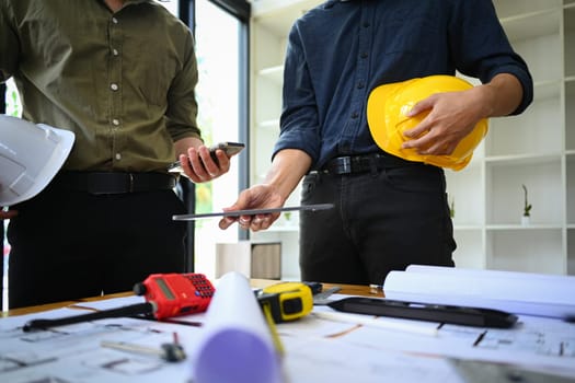 Cropped shot of two architect man using digital tablet, discussing work plan, industrial building design project at office.