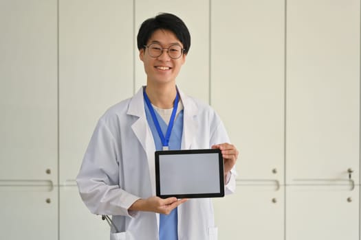 Doctor in white medical uniform holding and showing digital tablet with blank screen. Healthcare and medical concept.