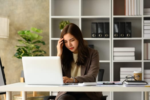 Upset asian businesswoman looking at laptop, frustrated about business failure in office.