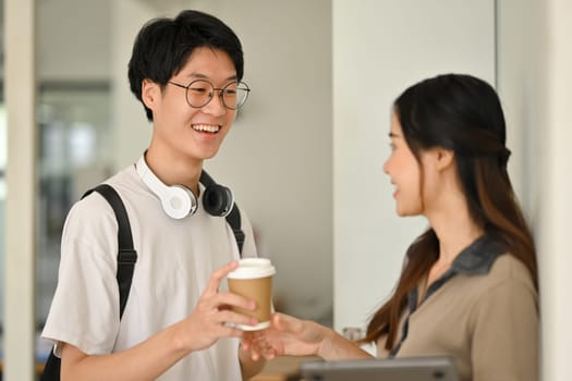 Smiling young college friends talking while standing at lockers in campus. Youth lifestyle concept.