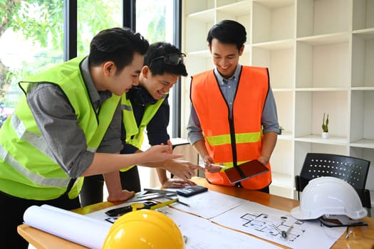 Image of architects team wearing reflective jackets collaborating, planning working together in meeting room.