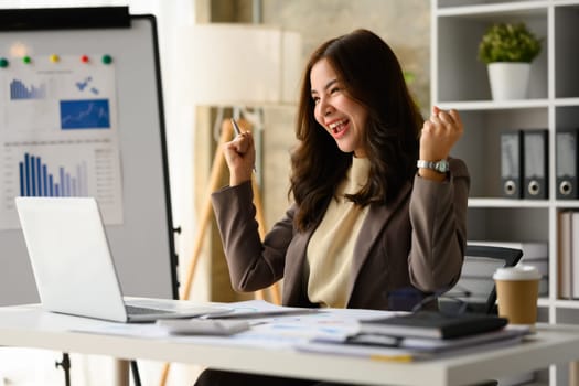 Surprised asian female entrepreneur looking at laptop screen, making winner yes gesture, celebrating business success.
