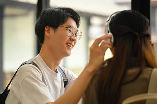 Happy moment of loving young asian man wearing headphones to his girlfriend. Lifestyle and love concept.
