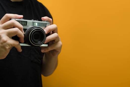 Man hands holding retro photo camera on yellow background with copy space.