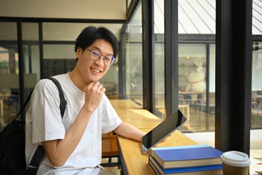 Portrait of asian man student in glasses sitting at coffee shop and using tablet. Education, learning and technology concept.
