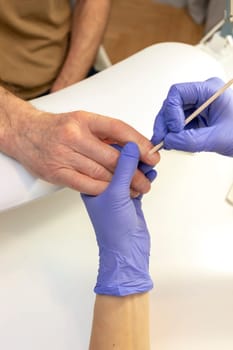 Man's hands on work station in manicure beauty salon. Nail professional doing mature male's nail treatment in spa, pushing cuticle back with orange stick. Safe eco Japanese mani. Vertical, closeup