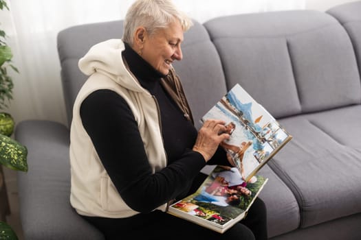 An elderly woman with nostalgia looks at old photos in a photo album or photobook - The concept of family and life values and loneliness in old age
