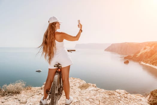A woman cyclist on a mountain bike looking at the landscape of mountains and sea. Rear view of cyclist woman standing in front to the sea with outstretched arms. Freedom and healthy lifestyle concept