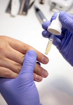 Cropped nail technician applies natural oil on cuticle, fingernails. Eco Japanese bio manicure. Safe organic nail treatment for adults, children, expectant moms. Vertical plane, closeup.