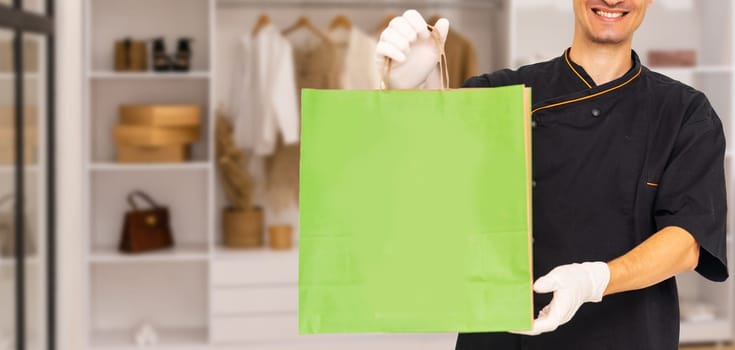 Young handsome delivery man holding paper bag with takeaway food happy with big smile