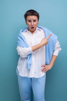 young indignant dude woman in casual look pointing finger to the side on blue studio background.