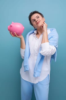 a pensive young woman with a short haircut holds a piggy bank and thinks where to invest the accumulated money.