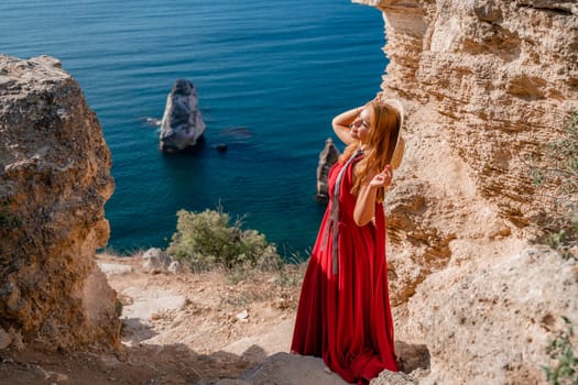 A woman in a flying red dress fluttering in the wind and a straw hat against the backdrop of the sea