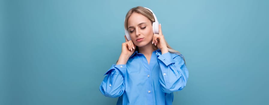 charming girl with pleasure listens to music in big headphones on a blue isolated background.