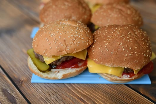 Several homemade burgers on a plastic cutting board and wooden background