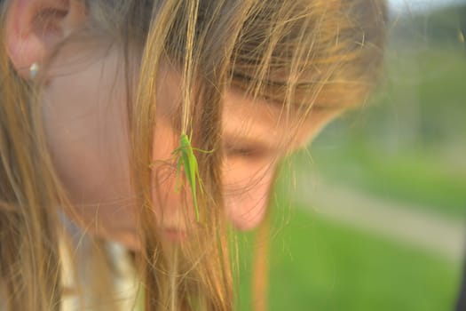 A little blonde girl with a grasshopper in her hair. The concept of romance and carefree childhood
