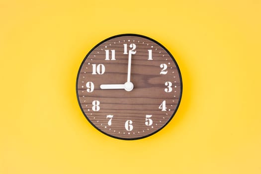 Retro wooden clock at 9 O' clock on yellow color background.