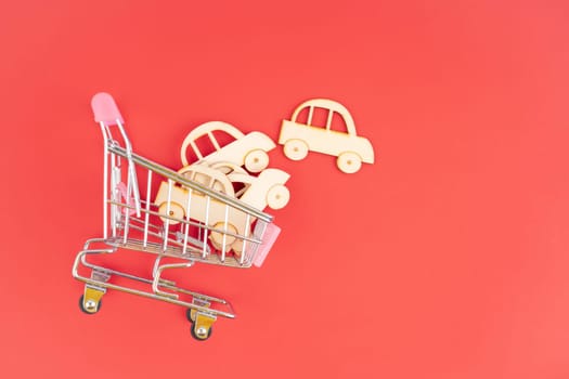 Wooden car model in the shopping cart on red background for buy car concept.