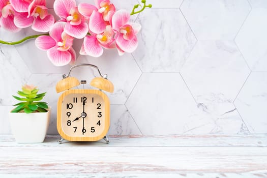 Wooden alarm clock and pink color orchid on wooden floor with copy space for your design.