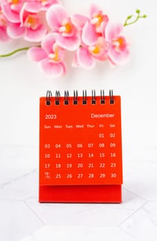 Red calendar December 2023. Desk calendar for year 2023 and pink orchid on marble background.