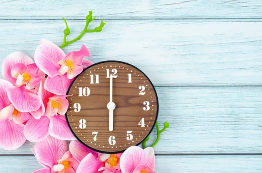 Wooden Alarm clock and pink streaked orchid flower on blue wooden background.