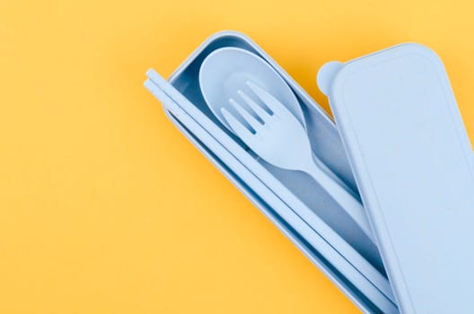 Plastic spoons, forks and chopsticks set on yellow background.