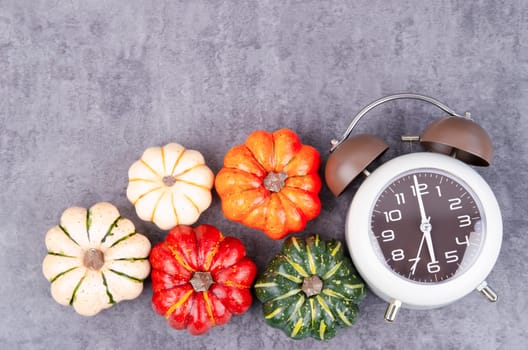 Top view of Pumpkins and an alarm clock on a rustic black table.