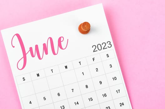 June 2023 calendar and wooden push pin on pink colour background.