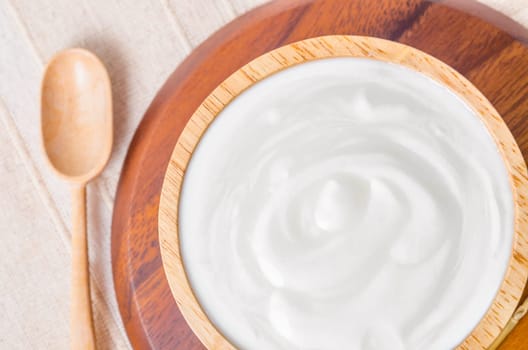 Greek yogurt in a wooden bowl and dry barley on table.