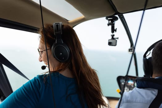 Smiling woman sitting in passenger seat in helicopter and looking down at the window. Mid shot