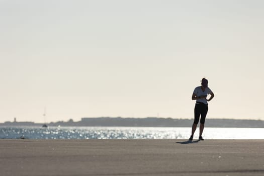 Silhouette of a woman standing on the shore at sunset and looking at her phone. Mid shot