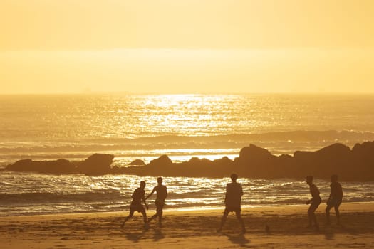 19 April 2023 Lisbon, Portugal: Costa da Caparica - young men playing ball on the beach at sunset. Mid shot
