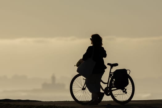 Silhouette of a woman with a bicycle at sunset. Mid shot